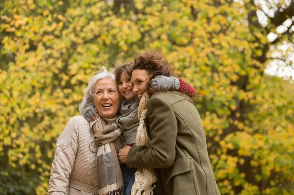 Une petite fille, sa maman et sa grand-mère sourient à l'extérieur